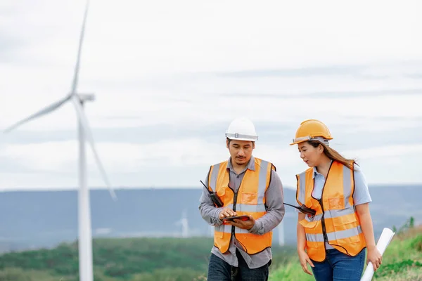 stock image Male and female engineers working on a wind farm atop a hill or mountain in the rural. Progressive ideal for the future production of renewable, sustainable energy.