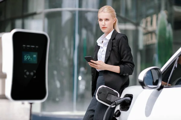 Businesswoman Wearing Black Suit Using Smartphone Leaning Electric Car Recharge — Foto Stock