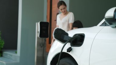 Evde şarj edilen elektrikli bir araçla okuldan yeni dönen anne ve kızın ilerici yaşam tarzı. Elektrikli araç, sürdürülebilir temiz enerjiyle çalışıyor..