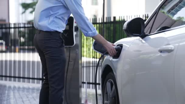 市内中心部を走行する前に 充電ステーションから彼の電気自動車に充電器プラグをインストール進歩的なビジネスマン 持続可能でクリーンなエネルギーを動力とする環境に優しい充電式車 — ストック動画