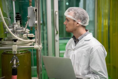Eczacı bilimadamı CBD yağ çıkarıcısından bilgi kaydetmek için dizüstü bilgisayar ve tıbbi esrar ürünleri üretmek için kullanılan bilimsel bir makine kullanıyor..