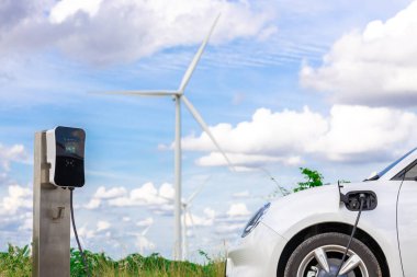 Progressive combination of wind turbine and EV car, future energy infrastructure. Electric vehicle being charged at charging station powered by renewable energy from wind turbine in the countryside.