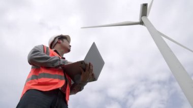 Gökyüzü arka planına sahip bir rüzgar türbini üzerinde çalışan mühendis. Yenilenebilir ve sürdürülebilir enerjinin gelecekteki üretimi için yenilikçi bir ideal. Rüzgar türbininden enerji üretimi.