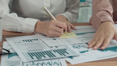 Ofis masasında çalışan iki hevesli genç iş kadını, veri tablosu raporlarıyla birlikte. Genç meslektaşlar istatistik veri kağıdı planları ve stratejisini tartışıyor ve analiz ediyorlar.