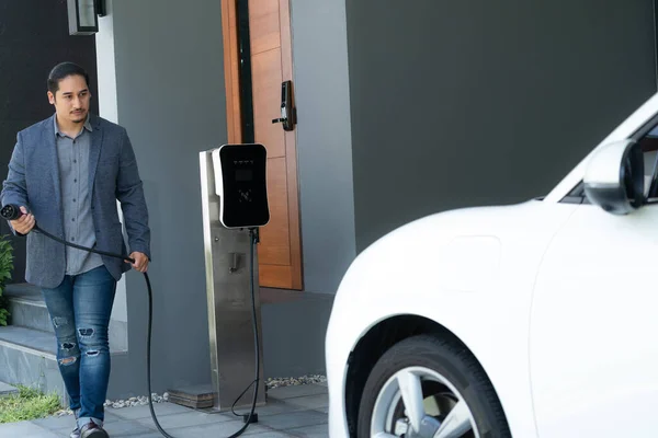 Progressive Asian Man Install Cable Plug His Electric Car Home — стоковое фото