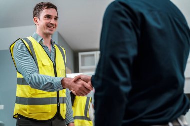 An engineer with a protective vest handshake with an investor in his office. Following a successful meeting, employee and employer form a partnership.