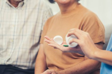 Contented senior woman sit along side with her husband, taking medicines while her caregiver advising her medication. Medication for seniors, nursing house, healthcare at home.