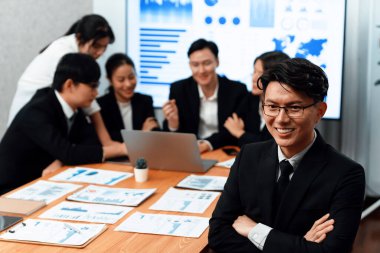 Focus portrait of successful confident male manager or executive in business wear with blurred background of businesspeople, colleagues working with financial report papers in office of harmony.