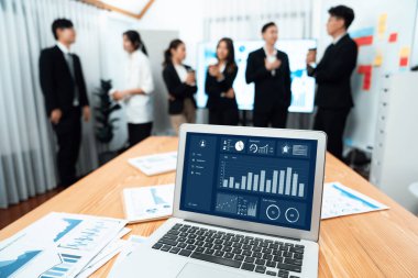 Focus laptop monitor display dashboard report by business intelligence, analyzed financial data for planning market strategy with blur background of standing office worker discussing in harmony office