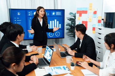 Confidence and young asian businesswoman give presentation on financial business strategy in dashboard report display on screen to colleagues in conference room meeting as harmony in workplace concept