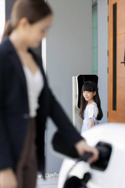 Evde şarj edilen elektrikli bir araçla okuldan yeni dönen anne ve kızın ilerici yaşam tarzı. Elektrikli araç, sürdürülebilir temiz enerjiyle çalışıyor..