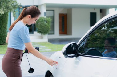 Progressive woman install cable plug to her electric car with home charging station. Concept of the use of electric vehicles in a progressive lifestyle contributes to clean environment.