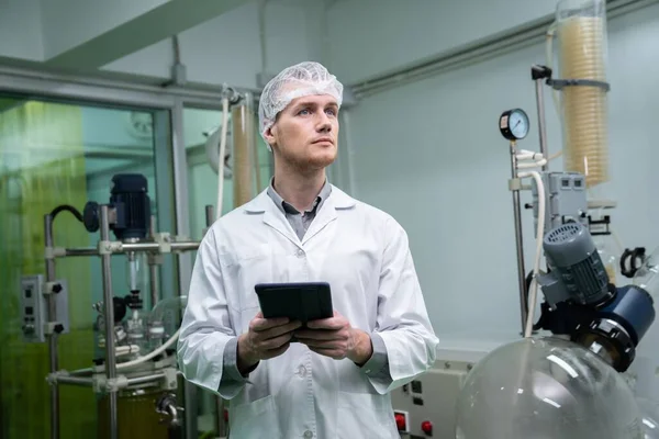 Male scientist, apothecary working in a laboratory for cannabis extraction while carrying a tablet containing extracted chemistry data from hemp leaf and cannabis plants. Medicinal cannabis extraction