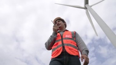 Gökyüzü arka planına sahip bir rüzgar türbini üzerinde çalışan mühendis. Yenilenebilir ve sürdürülebilir enerjinin gelecekteki üretimi için yenilikçi bir ideal. Rüzgar türbininden enerji üretimi.