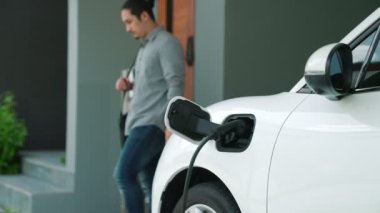 Adamın biri evinde elektrikli araç şarj aletinin fişini çekiyor. İlerici bir yaşam tarzında elektrikli araçların kullanımı, temiz ve sağlıklı bir çevreye katkıda bulunur..