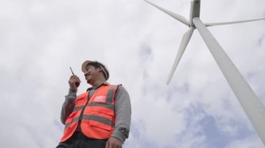Gökyüzü arka planına sahip bir rüzgar türbini üzerinde çalışan mühendis. Yenilenebilir ve sürdürülebilir enerjinin gelecekteki üretimi için yenilikçi bir ideal. Rüzgar türbininden enerji üretimi.