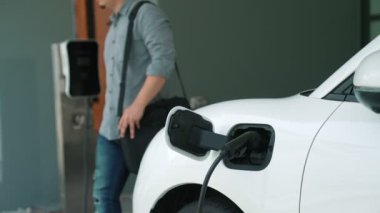 Adamın biri evinde elektrikli araç şarj aletinin fişini çekiyor. İlerici bir yaşam tarzında elektrikli araçların kullanımı, temiz ve sağlıklı bir çevreye katkıda bulunur..