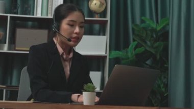 Kulaklık ve mikrofon takan iş kadını masasında çalışıyor ve dizüstü bilgisayar kullanıyor. Uzaktan kumandalı online toplantı için dizüstü bilgisayar kullanan hevesli kadın çalışanlar, ofiste iş videosu konferansı.