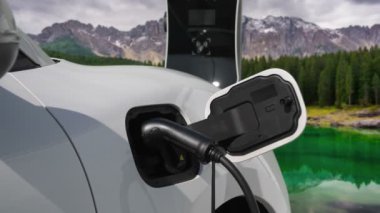 Temiz çevre için temiz enerjinin yol açtığı ilerici elektrikli araba kavramının arka planı olarak dağın tepesinde bulutun zaman kavramının yer aldığı doğal manzara. EV araba şarj istasyonunda şarj oluyor..