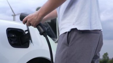 İlerici adam temiz çevre için rüzgar türbininin ürettiği temiz enerjiden güç alan EV arabasını şarj ediyor. Elektrikli araç rüzgar türbininden gelen enerji jeneratörüyle çalışıyor..