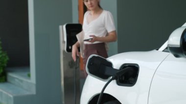 Evinde şarj edilen elektrikli bir araçla işten yeni dönen modern bir kadının ilerici yaşam tarzı. Elektrikli araç, sürdürülebilir temiz enerjiyle çalışıyor..