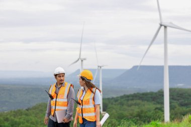 Erkek ve kadın mühendisler kırsal kesimdeki bir tepenin tepesinde ya da dağda rüzgar çiftliğinde çalışıyorlar. Yenilenebilir ve sürdürülebilir enerjinin gelecekteki üretimi için yenilikçi idealler.