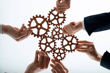 Hand holding wooden gear by businesspeople wearing suit for harmony synergy in office workplace concept. Isolated background. Bottom view of people hand make chain of gear into collective unity symbol