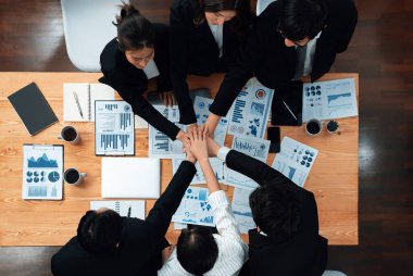 Top view cohesive group of business people join hands together, form circle over table filled with financial report paper. Colleagues working to promote harmony and team building concept in workplace.