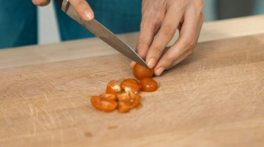 Close up hands holding a knife preparing a contented meal. Sliced tomatoes and other vegetables on the glass dish.