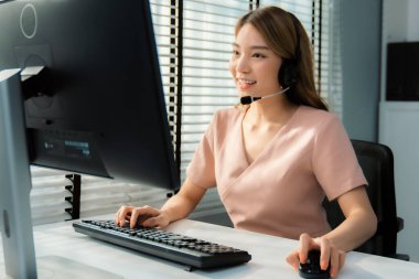 Competent female operator working on computer and while talking with clients. Concept relevant to both call centers and customer service offices.