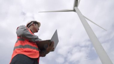 Gökyüzü arka planına sahip bir rüzgar türbini üzerinde çalışan mühendis. Yenilenebilir ve sürdürülebilir enerjinin gelecekteki üretimi için yenilikçi bir ideal. Rüzgar türbininden enerji üretimi.