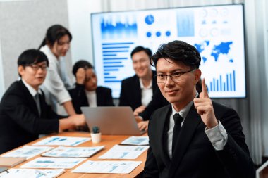 Focus portrait of successful confident male manager or executive in business wear with blurred background of businesspeople, colleagues working with financial report papers in office of harmony.