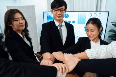 Business team of suit-clad businessmen and women join hands stack together and form circle. Colleagues collaborate and working together to promote harmony and teamwork unity in office workplace.