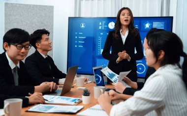 Confidence and young asian businesswoman give presentation on financial business strategy in dashboard report display on screen to colleagues in conference room meeting as harmony in workplace concept