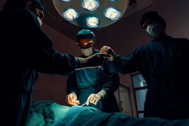 Steril ameliyathanedeki hastaya ameliyat yapan cerrahi ekip. Bir lambanın yaktığı ameliyathanede, profesyonel ve kendinden emin bir cerrahi ekip bilinçsiz bir hastaya tıbbi bakım sağlar..