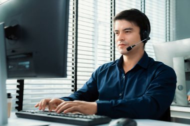 Young competent asian male call center agent working at his computer while simultaneously speaking with customers. Concept of an operator, customer service agent working in the office with headset.