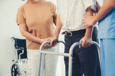 Contented senior man walking as he is helped by his wife and caretaker, walking with the aid of a folding walker. Nursing home for the elderly concept.