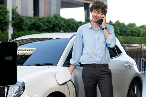 Progressive Businessman Talking Phone Leaning Electric Car Recharging Public Charging — Φωτογραφία Αρχείου