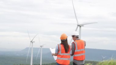 Erkek ve kadın mühendisler kırsal kesimdeki bir tepenin tepesinde ya da dağda rüzgar çiftliğinde çalışıyorlar. Yenilenebilir ve sürdürülebilir enerjinin gelecekteki üretimi için yenilikçi idealler.