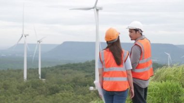 Erkek ve kadın mühendisler kırsal kesimdeki bir tepenin tepesinde ya da dağda rüzgar çiftliğinde çalışıyorlar. Yenilenebilir ve sürdürülebilir enerjinin gelecekteki üretimi için yenilikçi idealler.