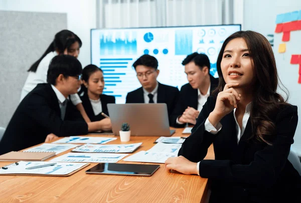 Focus portrait of female manger, businesswoman in the harmony meeting room with blurred of colleagues working together, analyzing financial paper report and dashboard data on screen in background.