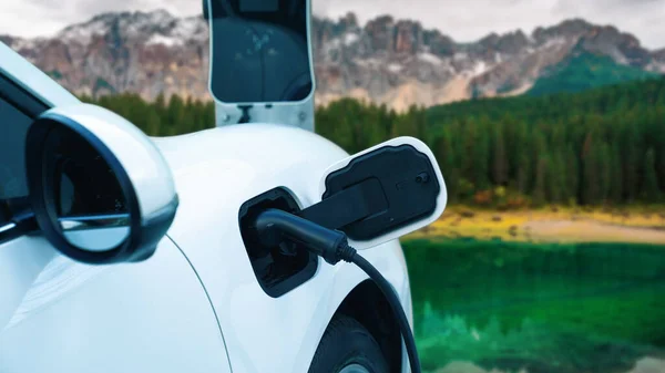 Energy sustainable car power by electro generator drive, recharge battery at charging station with mountain background for progressive travel concept. EV car in nature as symbol for clean environment.