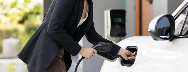 stock image Closeup progressive woman install cable plug to her electric car with home charging station. Concept of the use of electric vehicles in a progressive lifestyle contributes to clean environment.