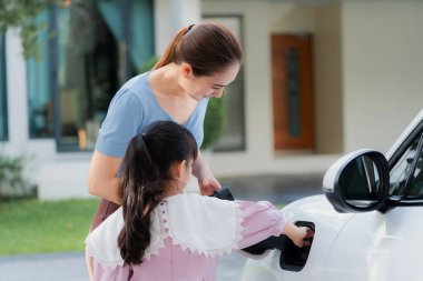 Evde şarj edilen elektrikli bir araçla okuldan yeni dönen anne ve kızın ilerici yaşam tarzı. Elektrikli araç, sürdürülebilir temiz enerjiyle çalışıyor..