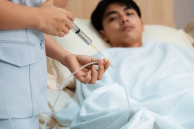 Doktor ve hemşire, hastanedeki steril odada hastaya tıbbi tedavi sağlayan serum tüpüne ilaç enjekte ediyor. Kırılgan hasta hasta hasta dinlenme odasında hasta yatağında tedavi görüyor..