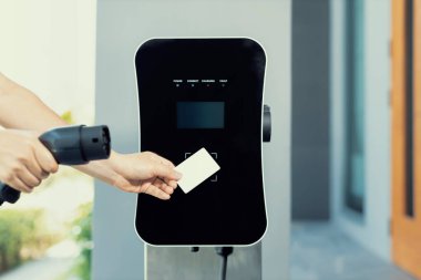 Hand holding credit card to pay public charging station and recharge her electric vehicle, symbolizing progressive lifestyle, combines e-wallet technology and sustainable transportation option.