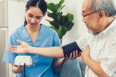 A contented retired man having a blood pressure check by his personal caregiver at his home with a smiley face. Senior care at home, nursing home for pensioners.