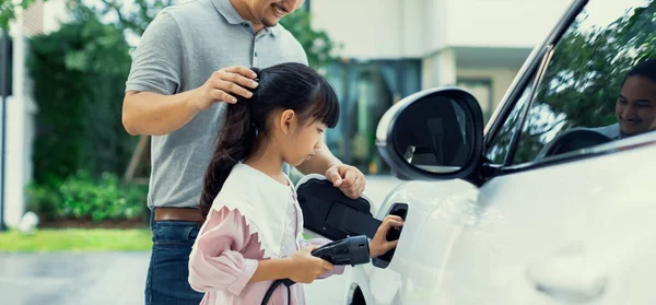 stock image Progressive father and daughter returned from school in electric vehicle that is being charged at home. Electric vehicle driven by renewable clean energy. Home charging station concept for environment