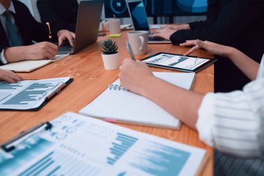 Closeup on BI dashboard on meeting desk with businesspeople analyzing or planning business strategy with hands pointing on financial paper reports as concept of harmony in office workplace.