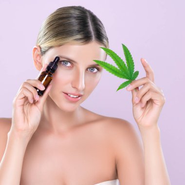 Cilt bakımı ürünleri için yeşil yaprak ve marihuana özlü şişe tutan pembe arka planda güzel bir kadının portresi. Kozmetik ve güzellik kavramları için kenevir CBD yağı.